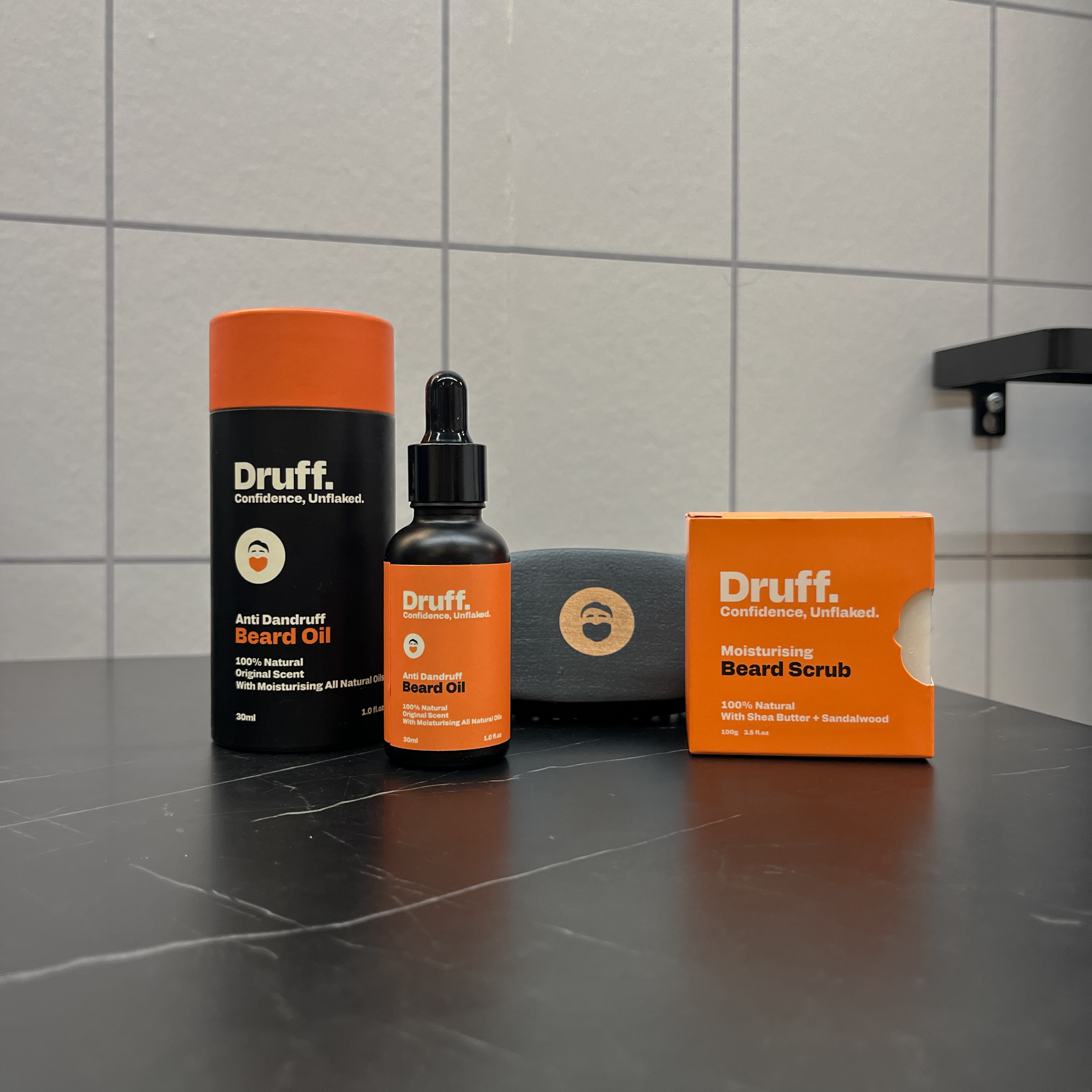 Druff beard care products including oil, scrub, and beard oil on a tiled bathroom counter.