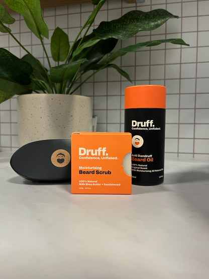 Druff beard care products including oil and scrub on a surface with a plant in the background.